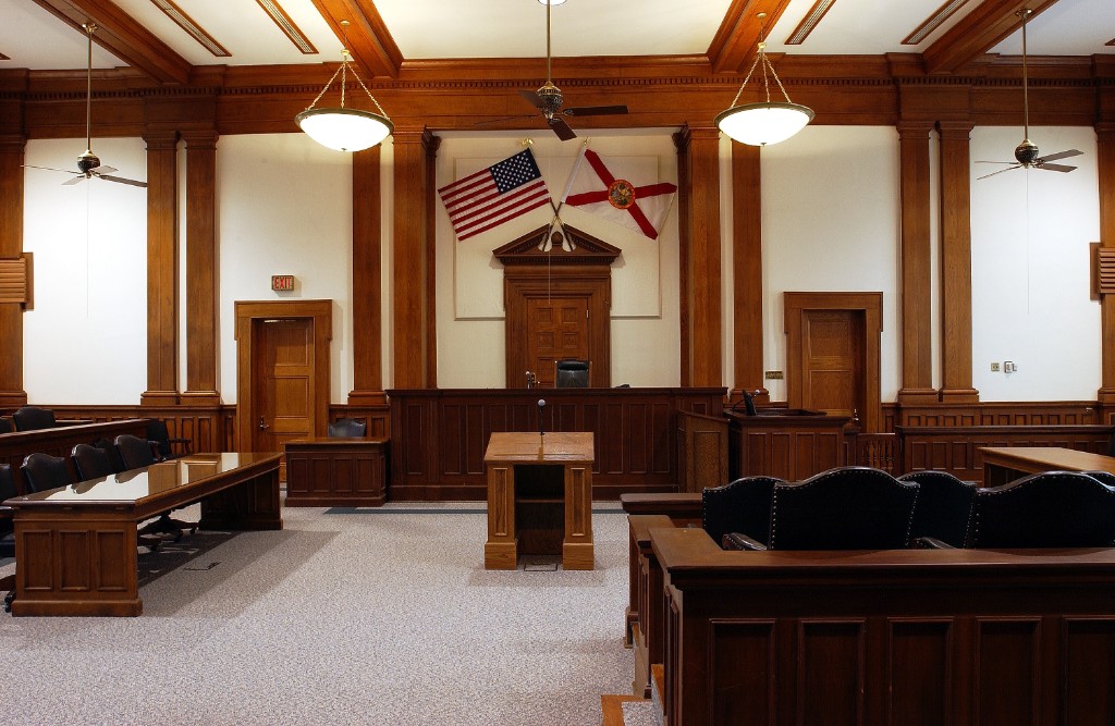 Formal wood-paneled courtroom interior viewed from the gallery toward the judge's bench and flags
